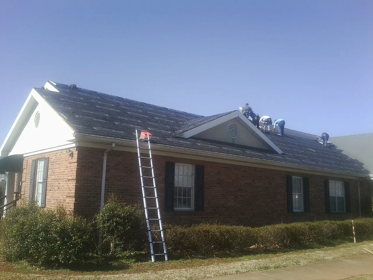 Crew tearing shingles off a brick ranch roof with a ladder set — Emergency Roof Repair work by our crew in Morris