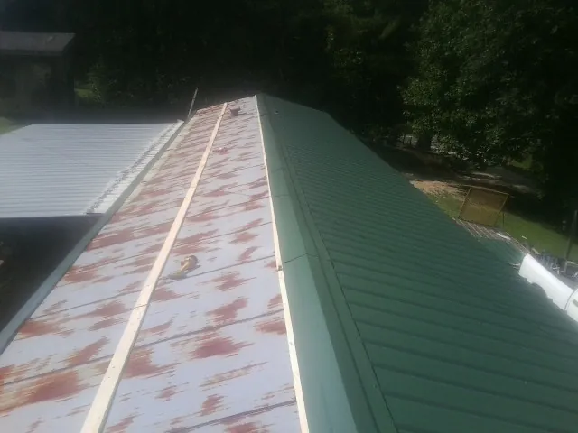 Old rusted panels beside newly installed green metal roofing — Wind Damage Roof Repair by Roofing Brothers in Morris