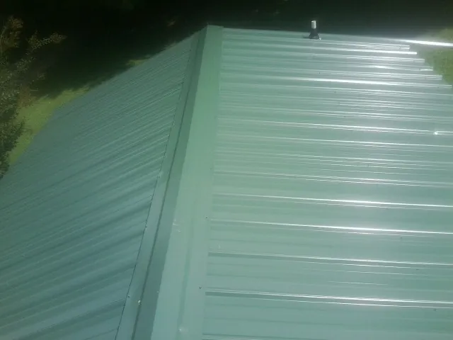 New green metal panels meeting at the ridge of a roof — Flat Roof Repair work by our crew in Morris